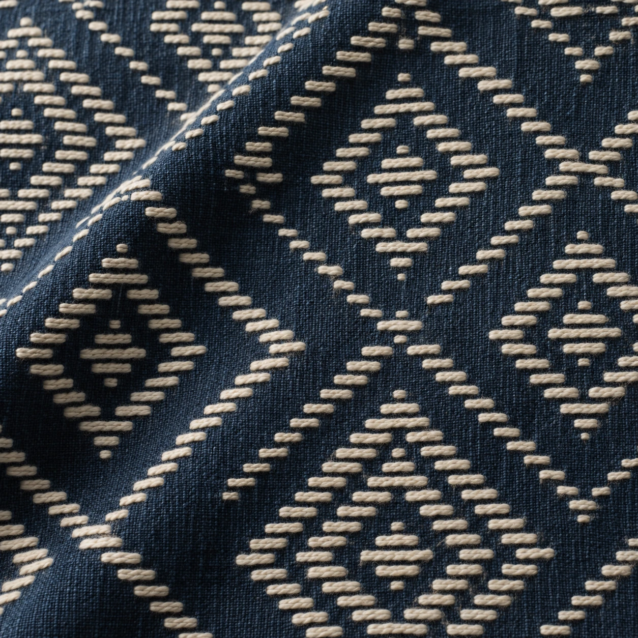 Close-up illustration of raised ivory cotton stitches forming stepped diamonds on indigo cloth.